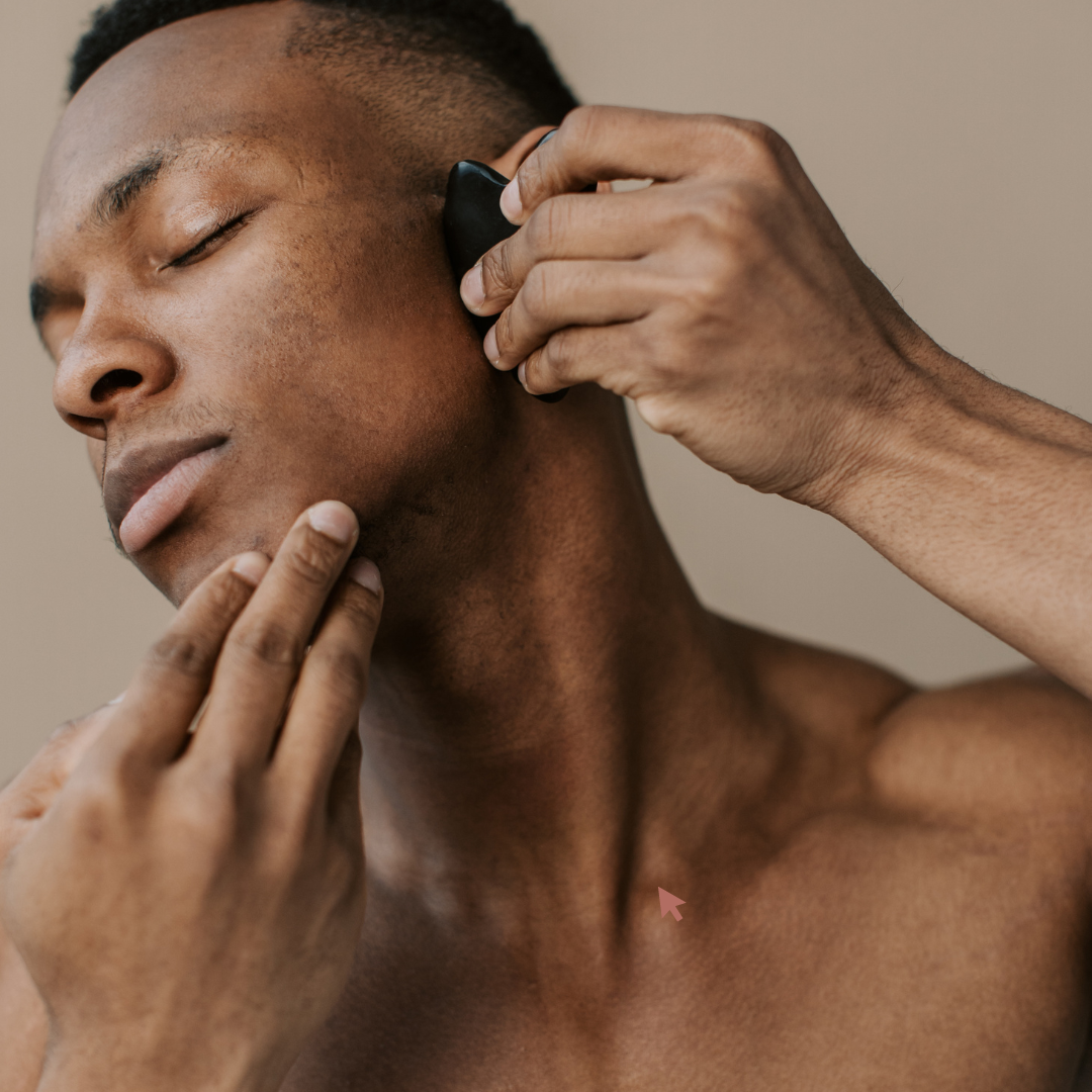 A black man using black gua sha facial massage tool on his face