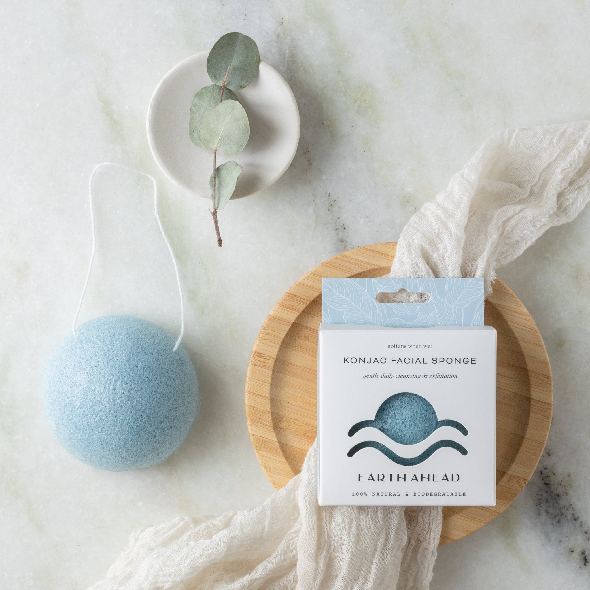 Blue konjac facial sponge beside its box on a bamboo dish
