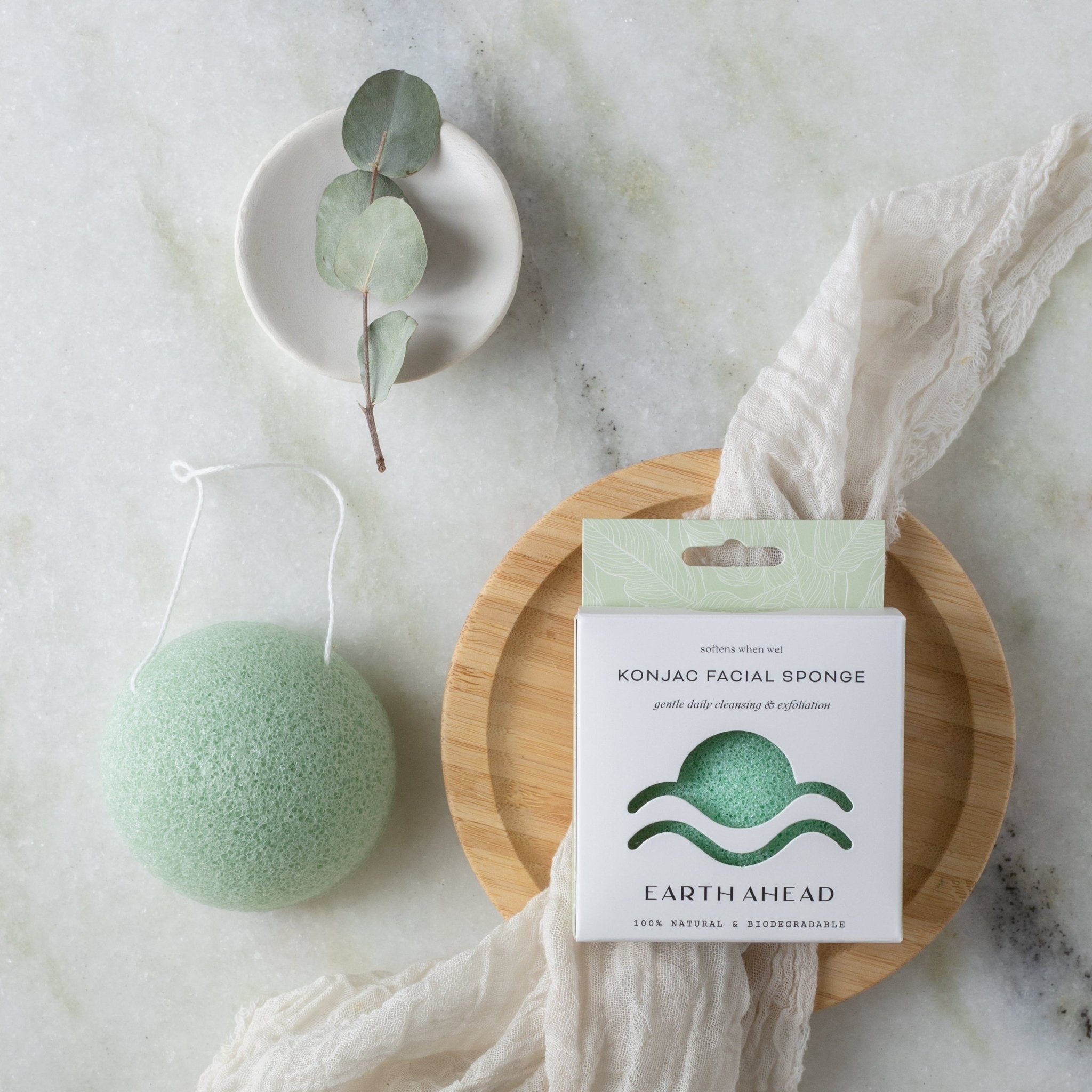 Earth Ahead konjac facial cleansing sponge in green,  beside its box on a marble flatlay
