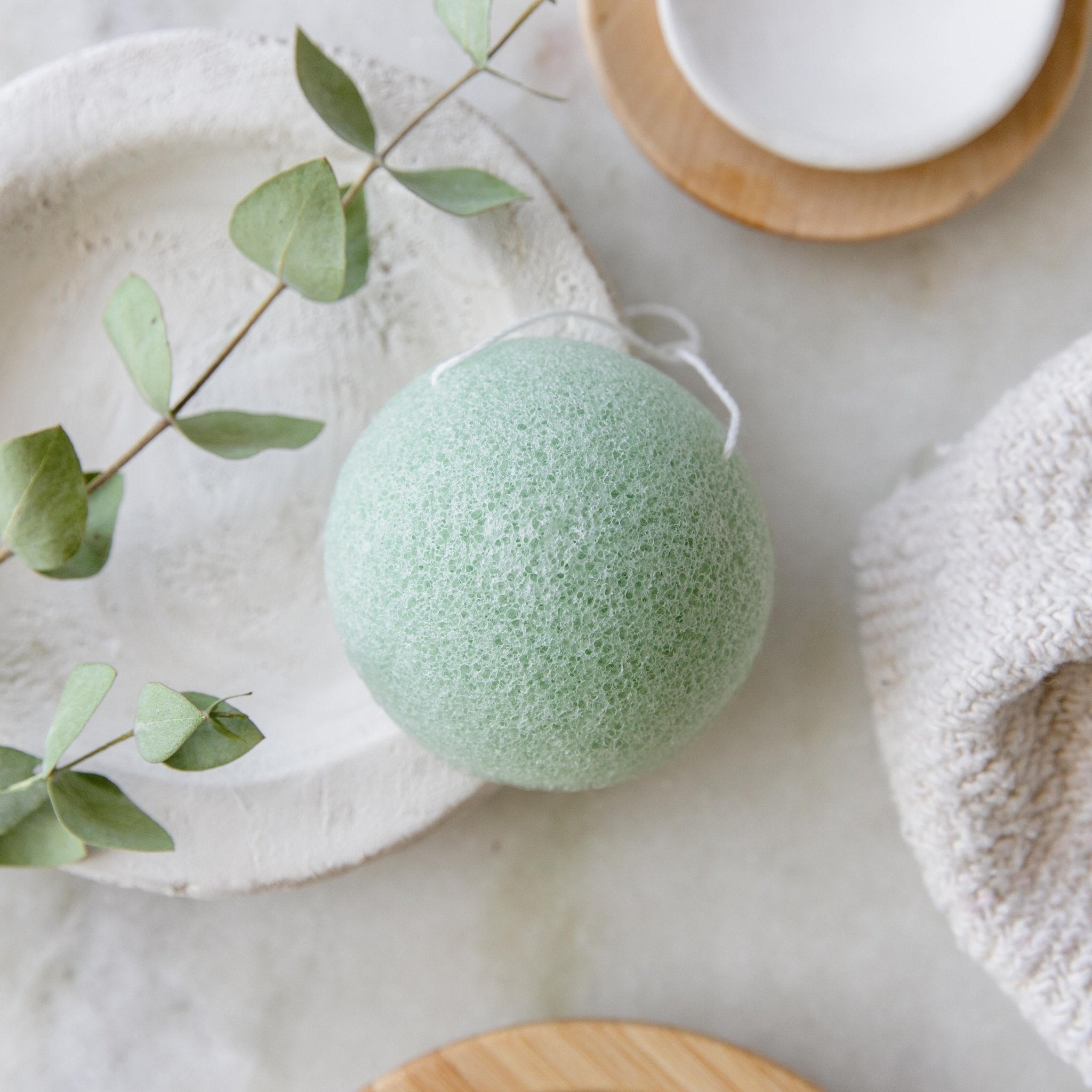 Green konjac facial sponge on a dish with eucalyptus and a towel