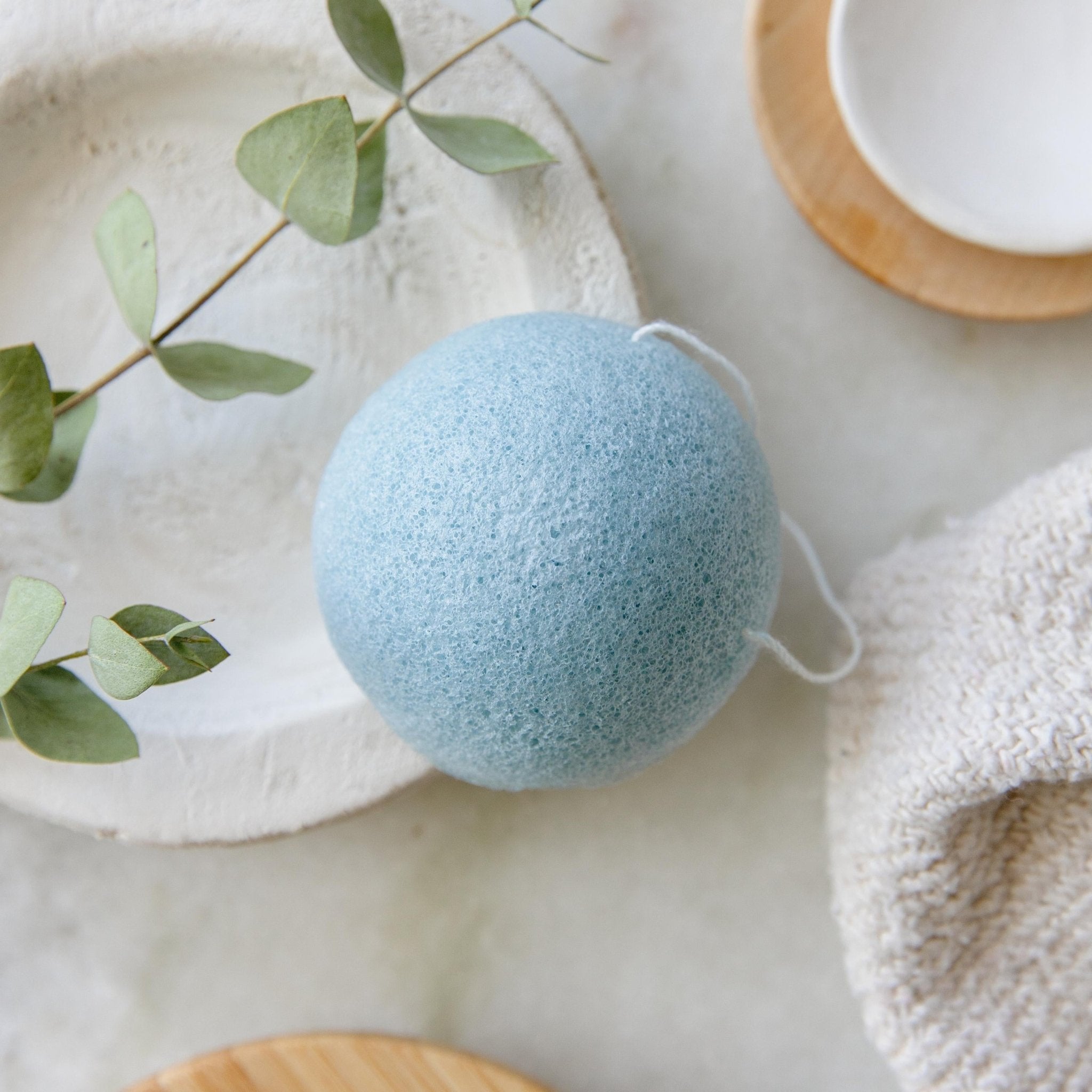 Blue konjac facial sponge on marble with eucalyptus