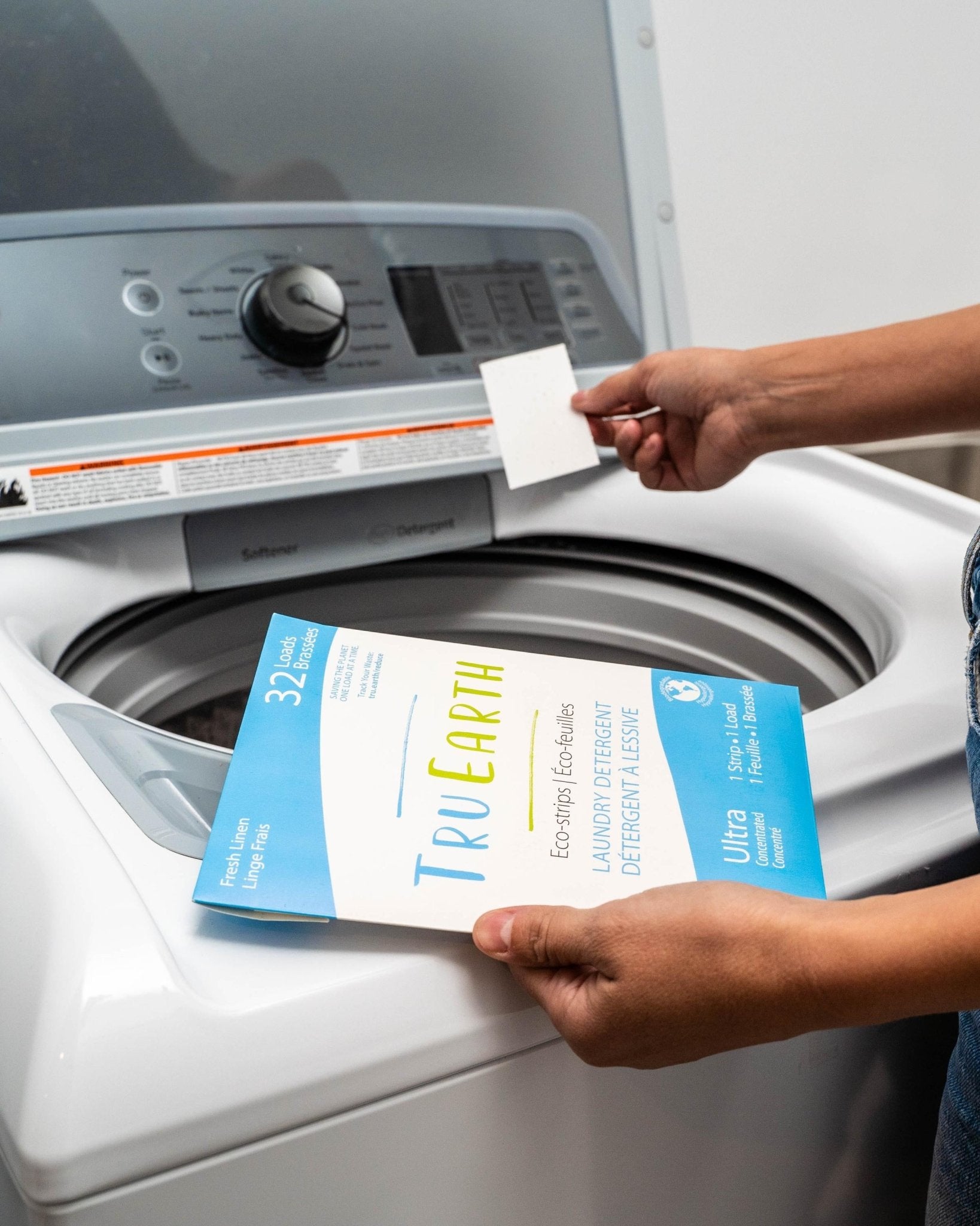 Hands putting TruEarth Laundry Detergent Strips into a laundry machine - Earth Ahead